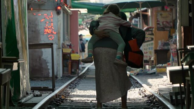 Gyeongamdong Railroad Town - Mother Carried Her Tired Daughter On Her Back While Walking On The Railroad Tracks In Gunsan, South Korea. - rear shot