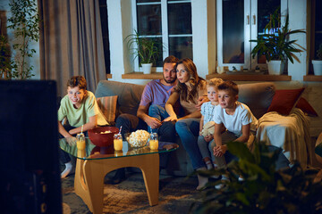 Hugging man and woman, parents sitting on couch with their children and watching tv in the evening. Family time. Concept of family, leisure time, relaxation, childhood and parenthood