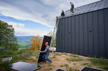 Technician building solar panel system on roof of house. Man worker in helmet carrying photovoltaic...