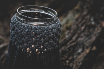 Jar with a burning candle decorated with knitted macrame fabric