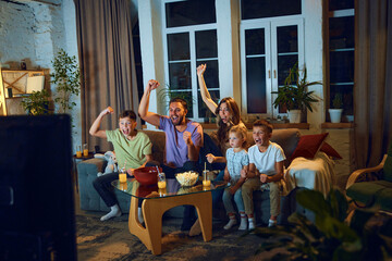 Emotional man, woman and children sitting on couch. Parents watching tv with children. Football match translation. Winning game. Concept of family, leisure time, relaxation, childhood and parenthood - obrazy, fototapety, plakaty