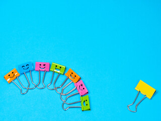 Lonely in team, not like everyone else, loneliness and difference. Funny smile metal binder clip. Multicolored paperclip on blue background with copyspace for text