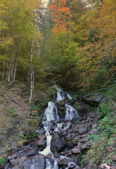 A mountain waterfall flows over the rocks. Waterfall cascade on mossy rocks in autumn