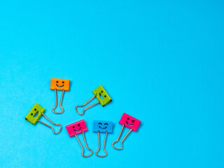 Multicolored funny smile metal binder clip or paperclip on blue background with copyspace for text