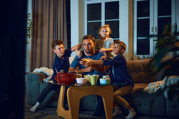 Fighting for tv controller. Father watching tv with his kids, sons and little daughter, sitting in...