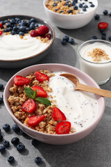 Bowls with yogurt and berries, wooden spoon and milk bottle on gray background