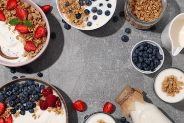 Bowls with yogurt and berries, wooden spoon and milk bottle on gray background, space for text