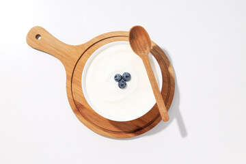 Bowl with yogurt with berries on board and wooden spoon on white background, top view