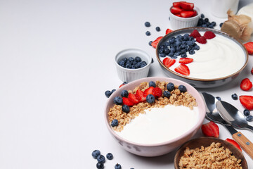 Bowls with yogurt and berries, spoons on white background, space for text