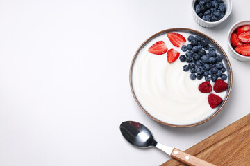 Bowls with yogurt and berries, spoon and board on white background, space for text