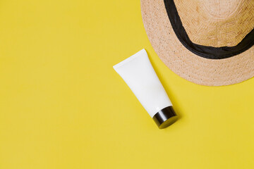Straw hat on a yellow background with white packaging of facial moisturizer. Space for text. Sombrero concept. Skin care concept.