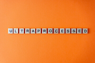 Word ultra processed. The phrase is laid out in wooden letters top view. Orange flat lay background