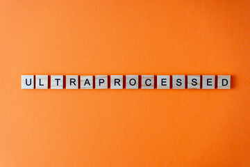 Word ultra processed. The phrase is laid out in wooden letters top view. Orange flat lay background