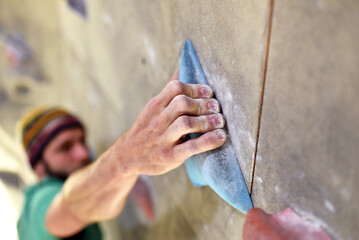 climber bouldering in a sports hall - holding on to the handle of an artificial rock wall - obrazy, fototapety, plakaty