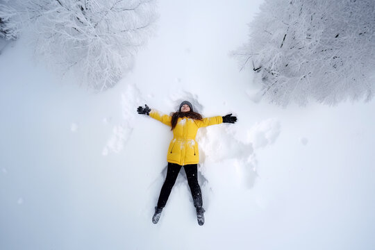 Young woman lies in the snow and makes a snow angel, arieal view