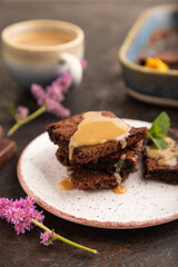 Chocolate brownie with caramel sauce with a cup of coffee on black concrete, side view, selective focus.
