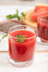 Watermelon juice with chia seeds and mint in glass on a white wooden background with linen textile. Side view, selective focus.