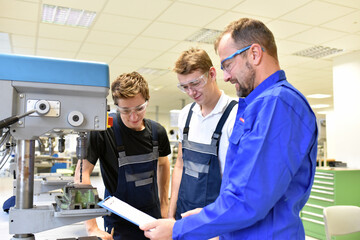 trainer and apprentice in technical vocational training at a drilling machine - obrazy, fototapety, plakaty