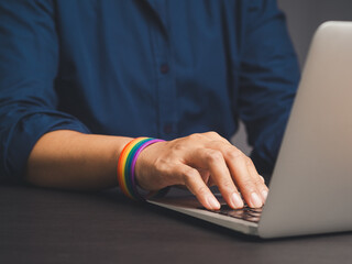 Hands typing on a laptop with a rainbow wristband while sitting at the table.