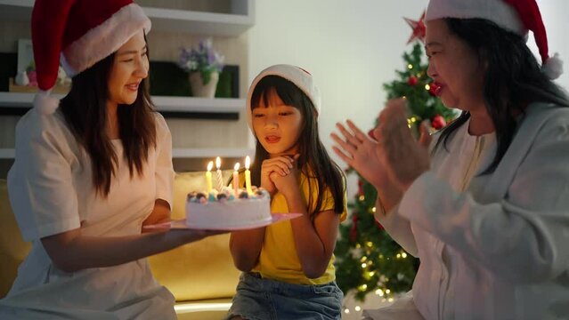 Happy Grandmother, mother holding cake and singing birthday song during celebration to little daughter at home. Happy little girl making wish, blowing candles during celebrating birthday with family