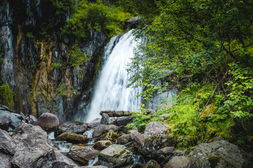 Fototapeta premium Korbu Waterfall is located on one of shores of Lake Teletskoye, Altai Republic, Siberia, Russia. Spring landscape, beautiful waterfall surrounded by trees and rocks, tourism place, nature environment