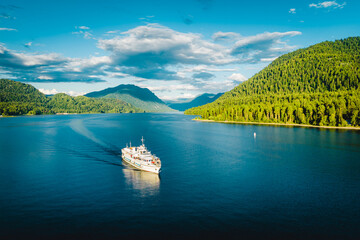 Summer Siberian landscape. Lake Teletskoye in Altai near Artybash. Boat with tourists. Mountains and forest around