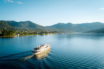 Summer Siberian landscape. Lake Teletskoye in Altai near Artybash. Boat with tourists. Mountains and forest around