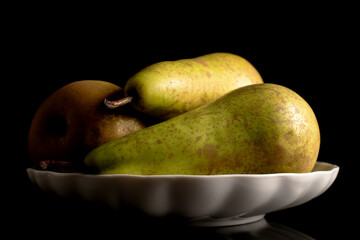 Three ripe pears on a white ceramic plate, macro, isolated on black background.