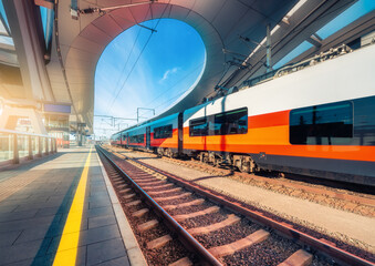 Obraz premium High speed train on the modern railway station at sunset in Graz, Austria. Beautiful orange intercity passenger train on the covered railway platform. Railroad. Passenger railway transportation