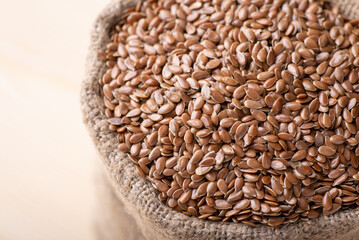 Linen seed in bag against wooden background. Close up of harvested linen grain, small seeds