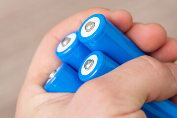 Hand of a man holding four blue 18650 batteries in hand. Using modern high capacity rechargeable...