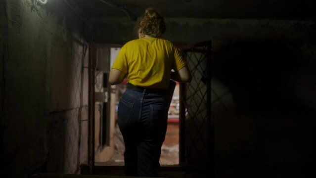 Following back shot of female plumber in dark basement heading to boiler room. Woman engineer walks through underground floor carrying toolkit