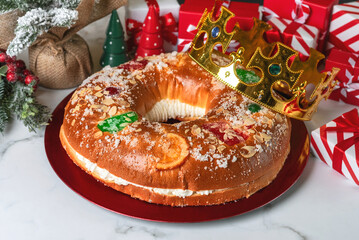 Roscon de reyes with cream and christmas ornaments on a red plate. Kings day concept spanish three...