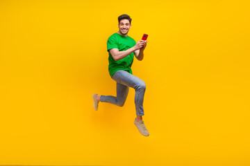Fototapeta na wymiar Full size photo of cool funny guy wear stylish t-shirt run to empty space with smartphone in hands isolated on yellow color background