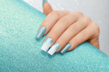 Female hand with long nails with glitter nail polish. Long blue nail design. Women hand with...