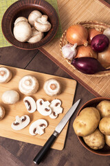 Fototapeta na wymiar Sliced mushrooms champignon on wooden cutting board with onion garlic and potato on kitchen. Cooking vegetarian vegan food