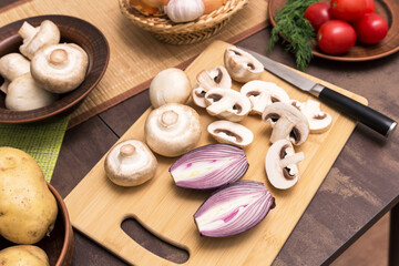 Sliced mushrooms champignon with red onion on wooden cutting board on kitchen table close up. Cooking vegetarian vegan food dish