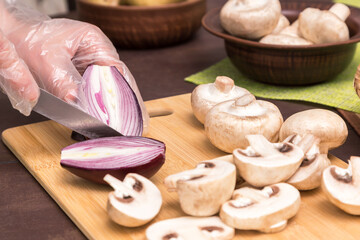 Obraz na płótnie Canvas Chef cutting, slicing red onion and mushrooms champignon close up. Hands in gloves cooking healthy vegetarian diet food