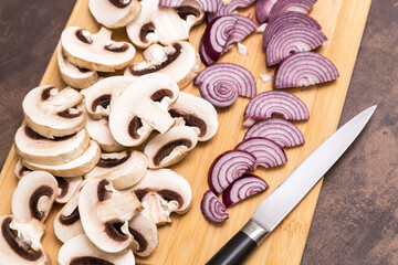 Sliced, cutting mushrooms champignon with red onion on wooden board with knife close up