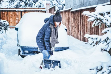 Fotobehang woman with shovel cleaning snow around car. Winter shoveling. Removing snow after blizzard © Melinda Nagy