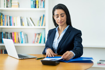 Serious hispanic mature businesswoman working with documents at desk