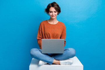 Full length photo of lovely young lady sit cube working remotely dressed stylish brown garment isolated on blue color background - obrazy, fototapety, plakaty