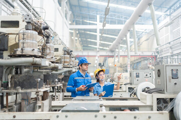 American male engineer and Asian female manager point to destination Wear a uniform and safety helmet. There are machines working in a factory, industrial business producing plastics and steel. - Powered by Adobe