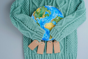 Sleeves of knitwear sweater hug the planet with tags. Responsible consumption clothes. Environmental friendliness and sustainable fashion. Zero waste - obrazy, fototapety, plakaty