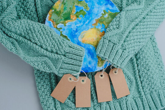 Sleeves of knitwear sweater hug the planet with tags. Responsible consumption clothes. Environmental friendliness and sustainable fashion.