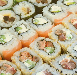 Close-up of a lot of sushi rolls with different fillings lie on a wooden surface. Macro shot of cooked classic Japanese food with a copy space.