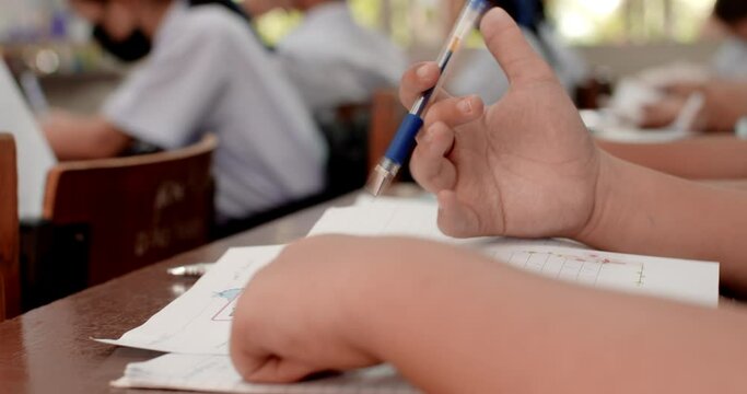 Cut-in shot while the Asian students in white uniforms are writing the answers on their papers in Asian school examination. 