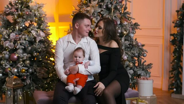 Family with newborn baby celebrate New Year winter holiday together at home. Concept of happy memories in childhood, Christas tree decoration, balls, garland light.