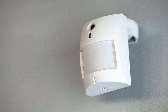 A white motion sensor camera on a gray wall, providing security and surveillance.