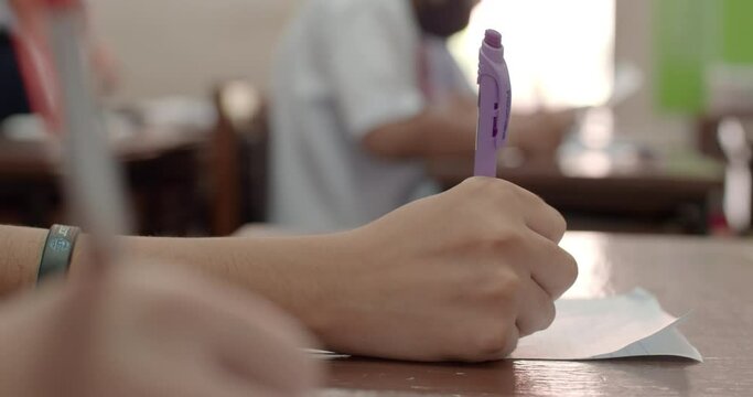 Cut-in shot while the Asian students in white uniforms are writing the answers on their papers in Asian school examination. 